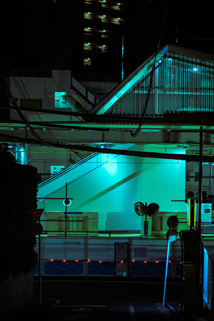 Side of a train station at night lit in a dark green blue.